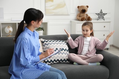 Photo of Psychologist having therapy session with little girl on sofa in office