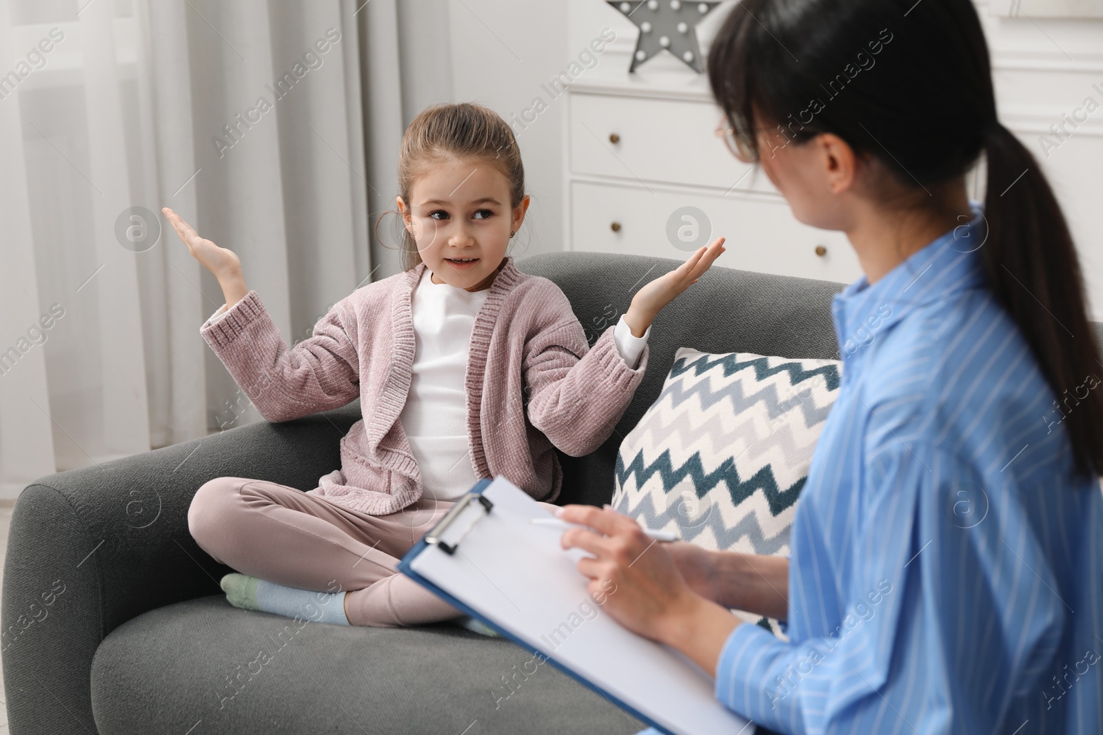 Photo of Psychologist having therapy session with little girl on sofa in office