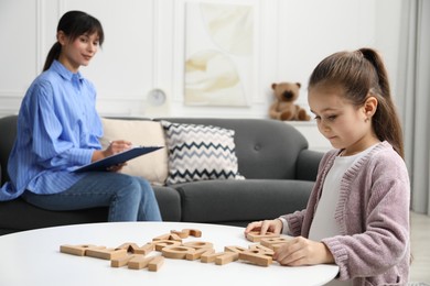 Photo of Girl playing with letters at table while psychologist taking notes, selective focus