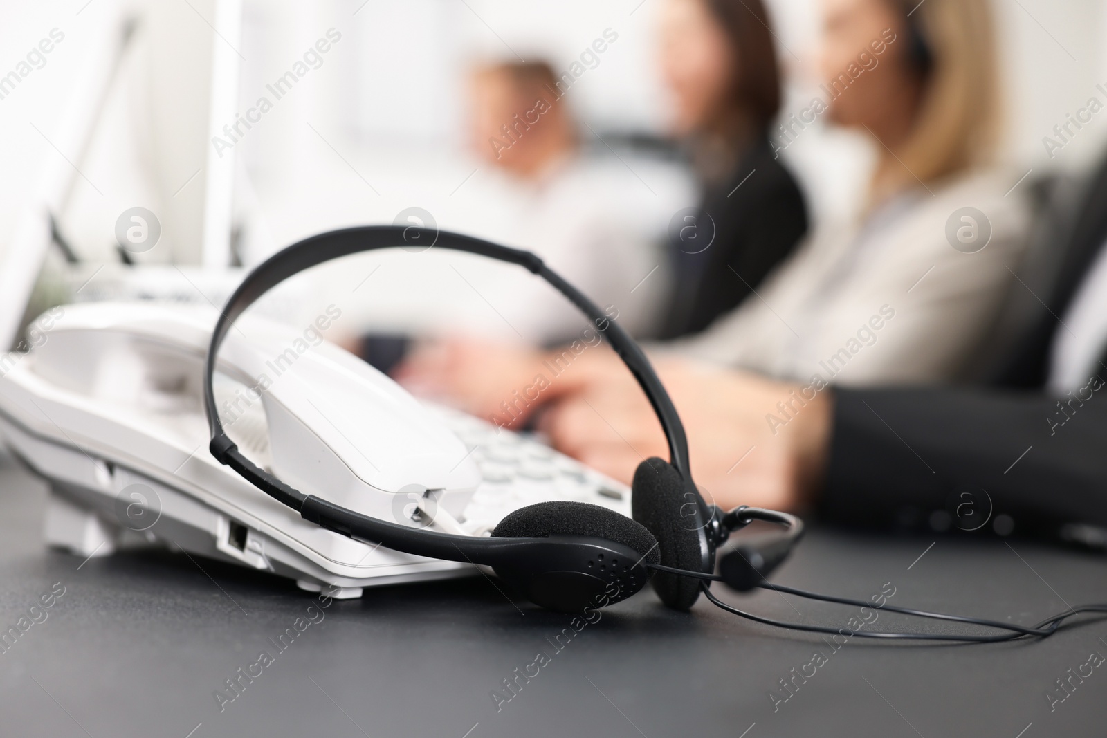 Photo of Technical support call center. Team of operators working at table in office, focus on phone and headset