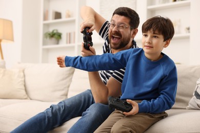 Photo of Father and his son playing video games on sofa in living room