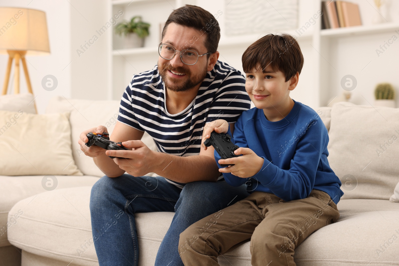 Photo of Father and his son playing video games on sofa in living room