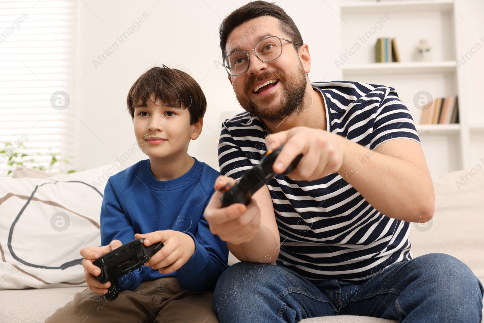 Photo of Father and his son playing video games on sofa in living room