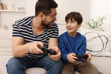 Photo of Father and his son playing video games on sofa in living room