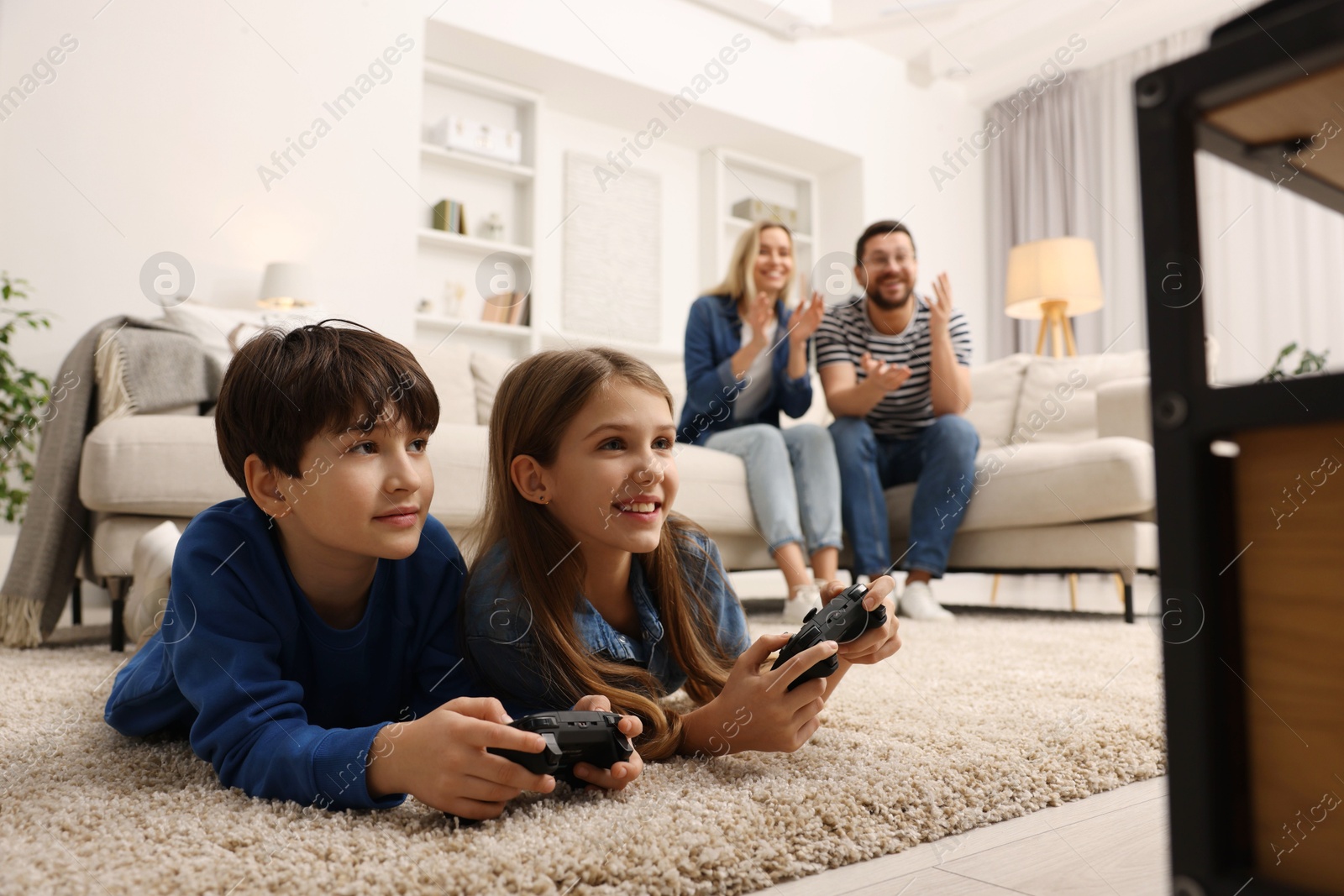 Photo of Cute kids playing video games while their parents resting on sofa at home, selective focus