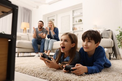 Photo of Cute kids playing video games while their parents resting on sofa at home, selective focus