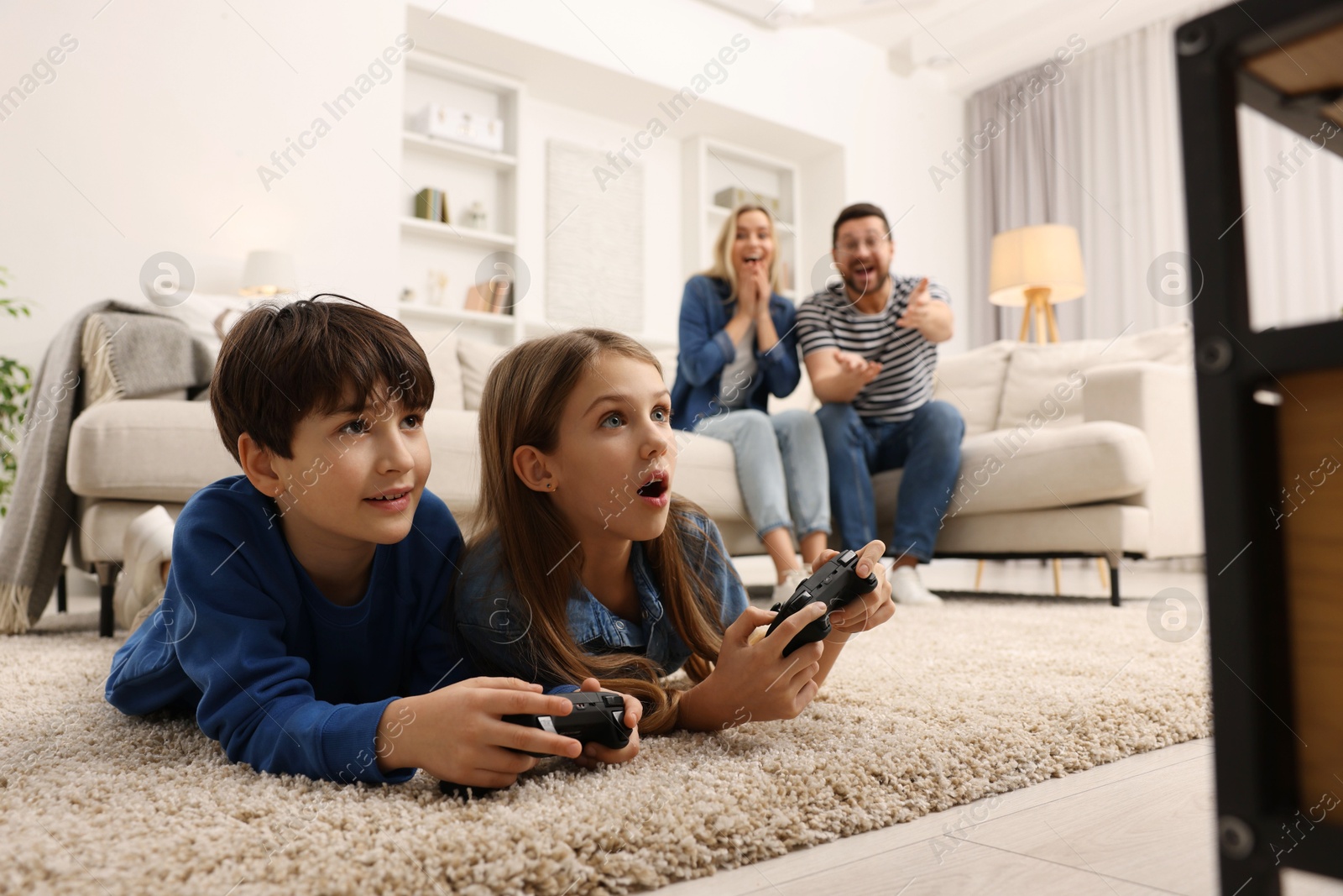 Photo of Cute kids playing video games while their parents resting on sofa at home, selective focus