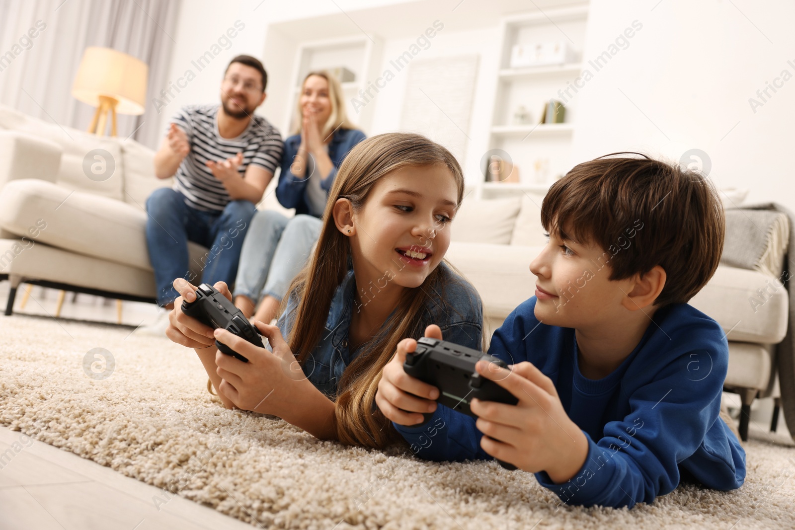 Photo of Cute kids playing video games while their parents resting on sofa at home, selective focus