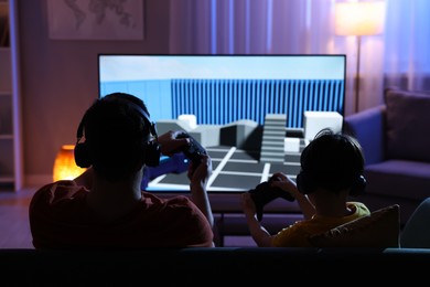 Photo of Father and his son playing video game on sofa in living room, back view