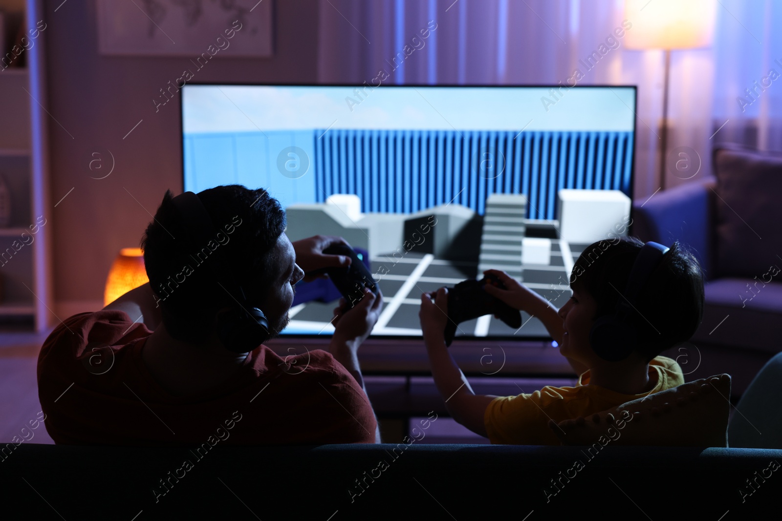 Photo of Father and his son playing video game on sofa in living room