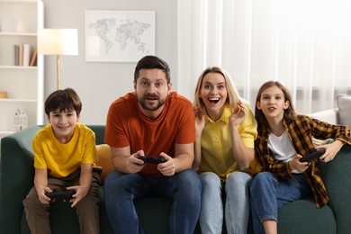 Photo of Happy family playing video games on sofa in living room