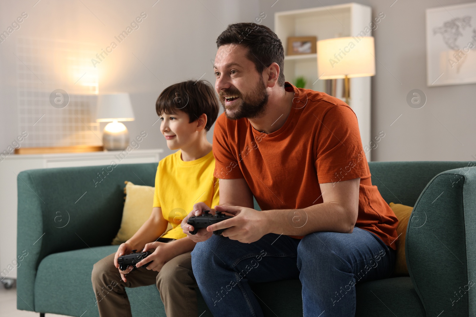 Photo of Happy father and his son playing video games on sofa in living room