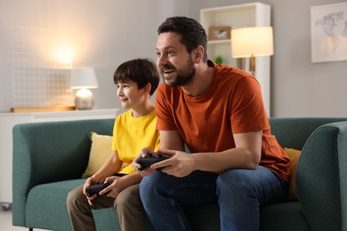 Photo of Happy father and his son playing video games on sofa in living room