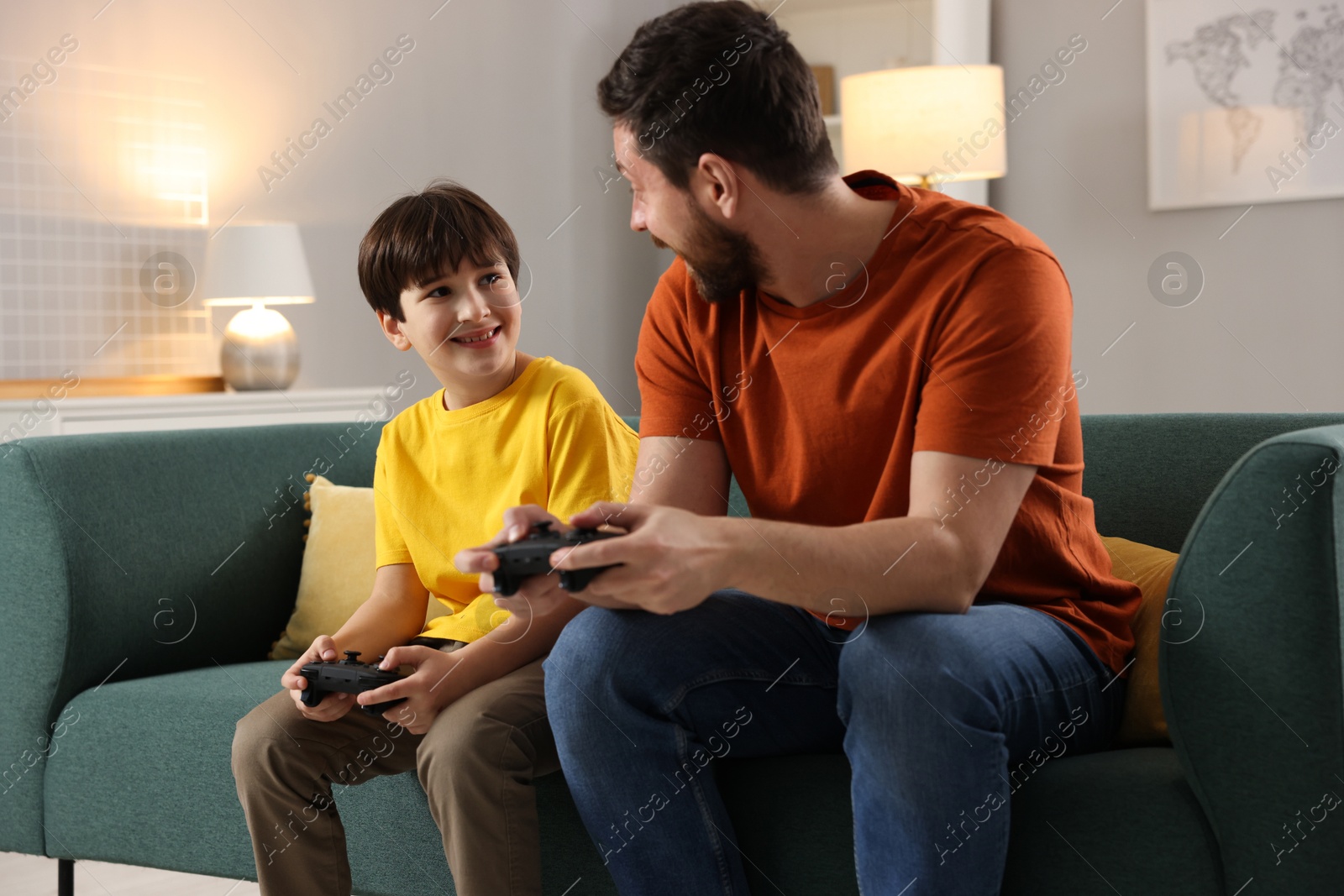 Photo of Happy father and his son playing video games on sofa in living room