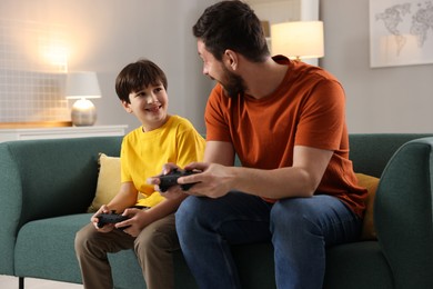 Photo of Happy father and his son playing video games on sofa in living room