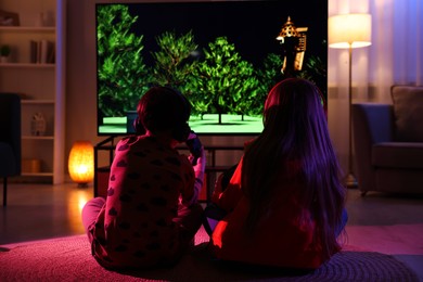 Photo of Little kids in headphones playing video game indoors at night, back view