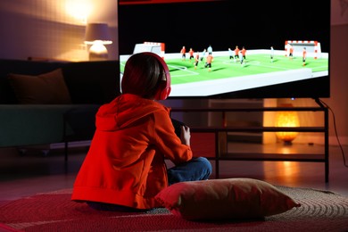 Photo of Little girl in headphones playing video game at home, back view