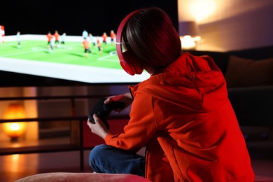 Photo of Little girl in headphones playing video game at home, back view