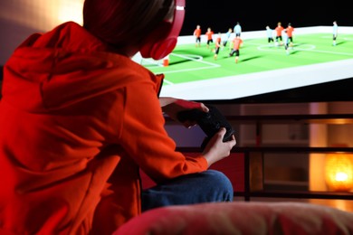 Photo of Little girl in headphones playing video game at home, closeup