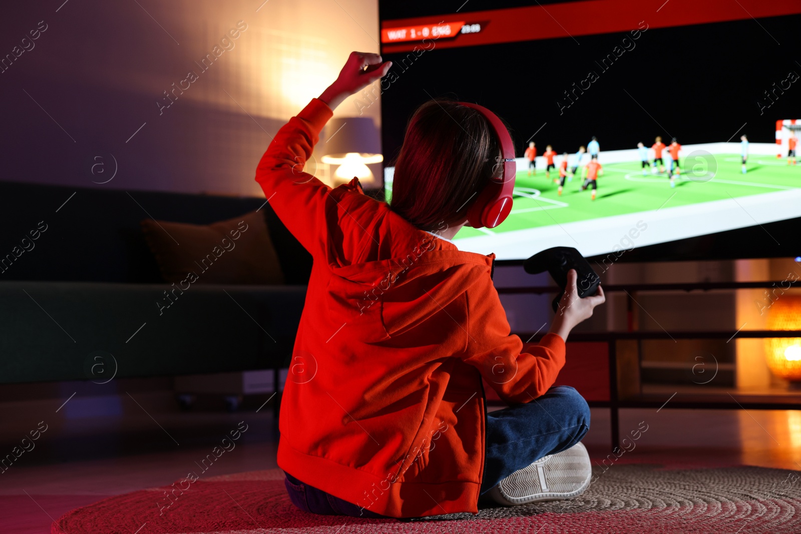 Photo of Little girl in headphones playing video game at home, back view