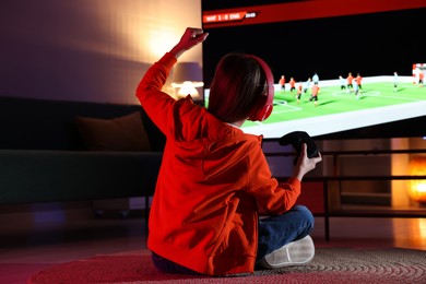 Photo of Little girl in headphones playing video game at home, back view