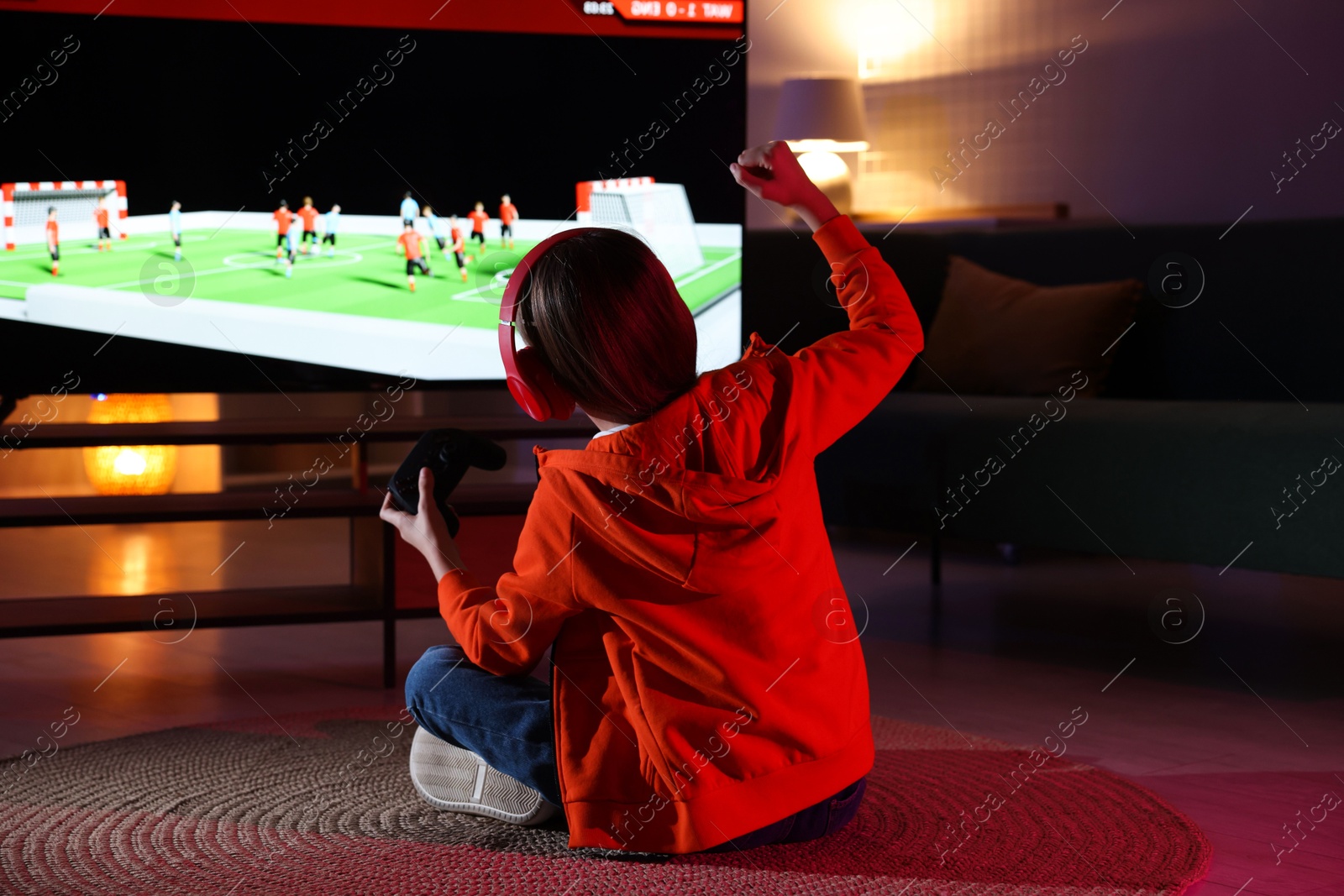 Photo of Little girl in headphones playing video game at home, back view