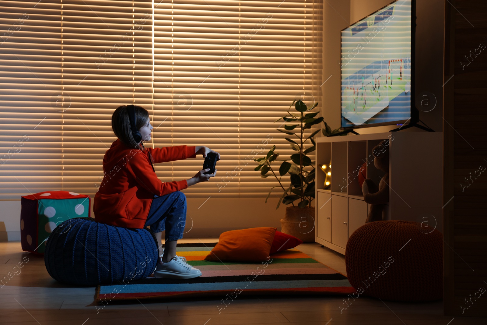 Photo of Little girl in headphones playing video game at home