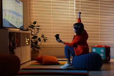 Photo of Little girl in headphones playing video game at home