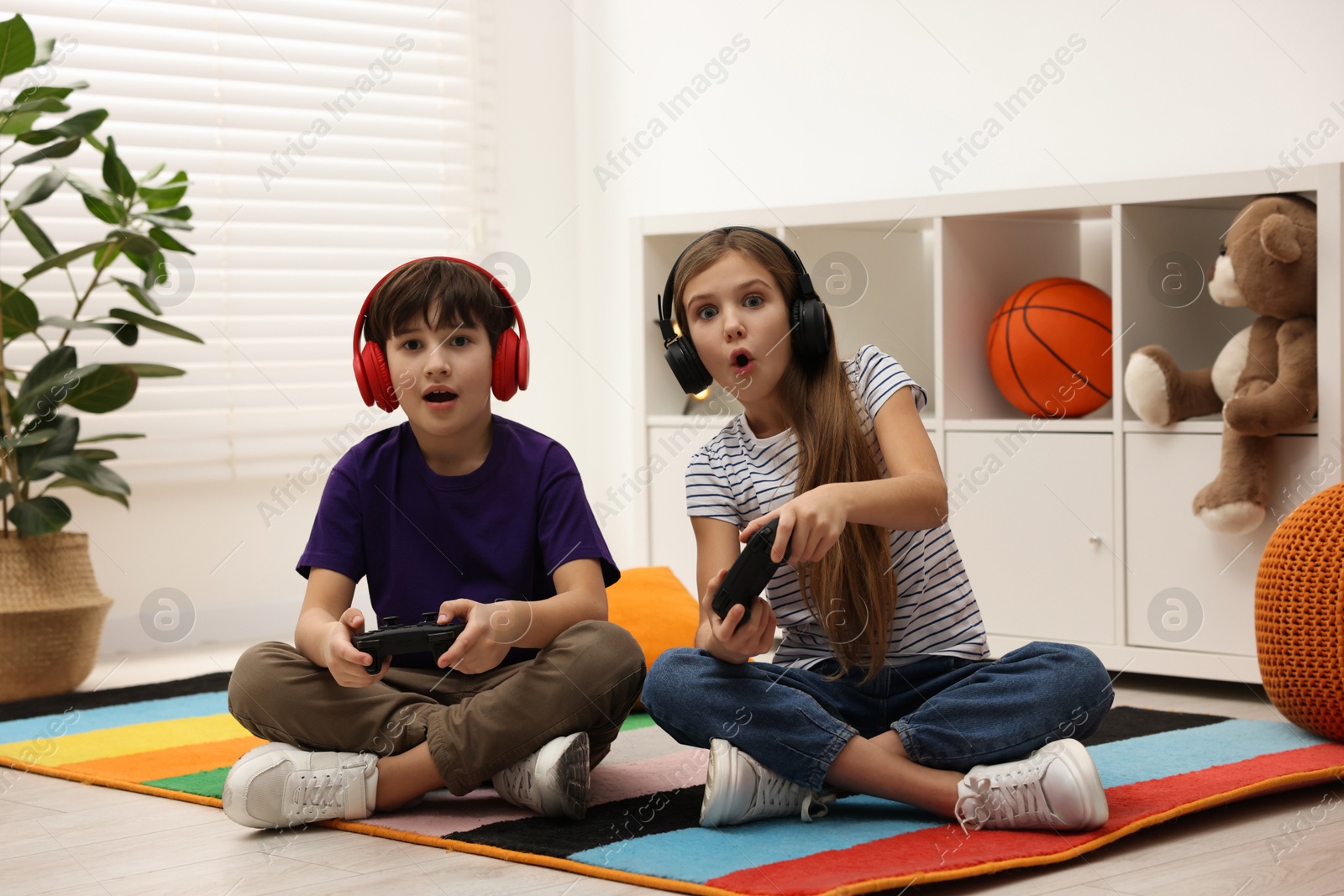 Photo of Cute kids in headphones playing video games on floor indoors