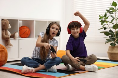 Photo of Cute kids in headphones playing video games on floor indoors