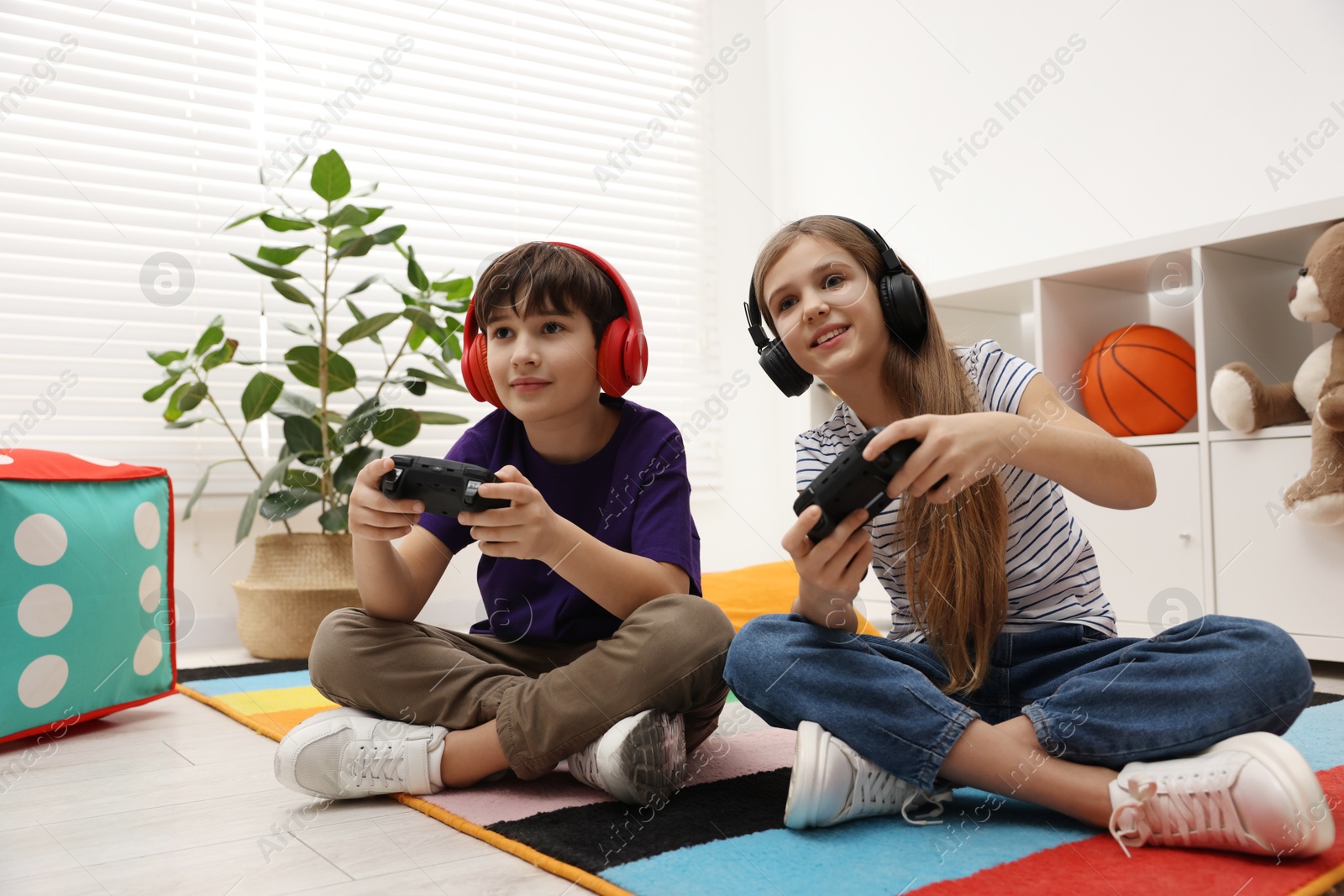 Photo of Cute kids in headphones playing video games on floor indoors