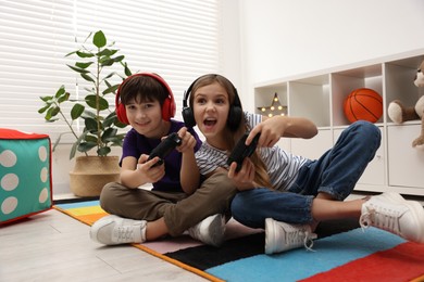 Photo of Cute kids in headphones playing video games on floor indoors