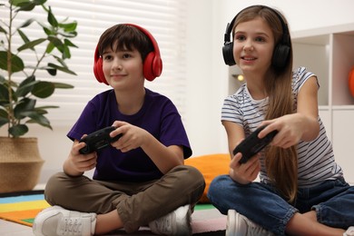 Photo of Cute kids in headphones playing video games on floor indoors