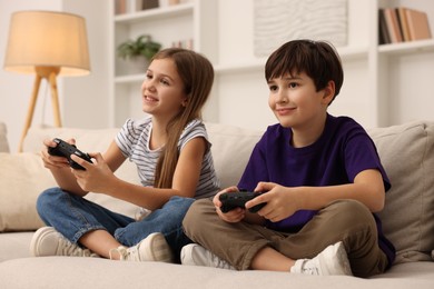 Photo of Cute kids playing video games on sofa in living room