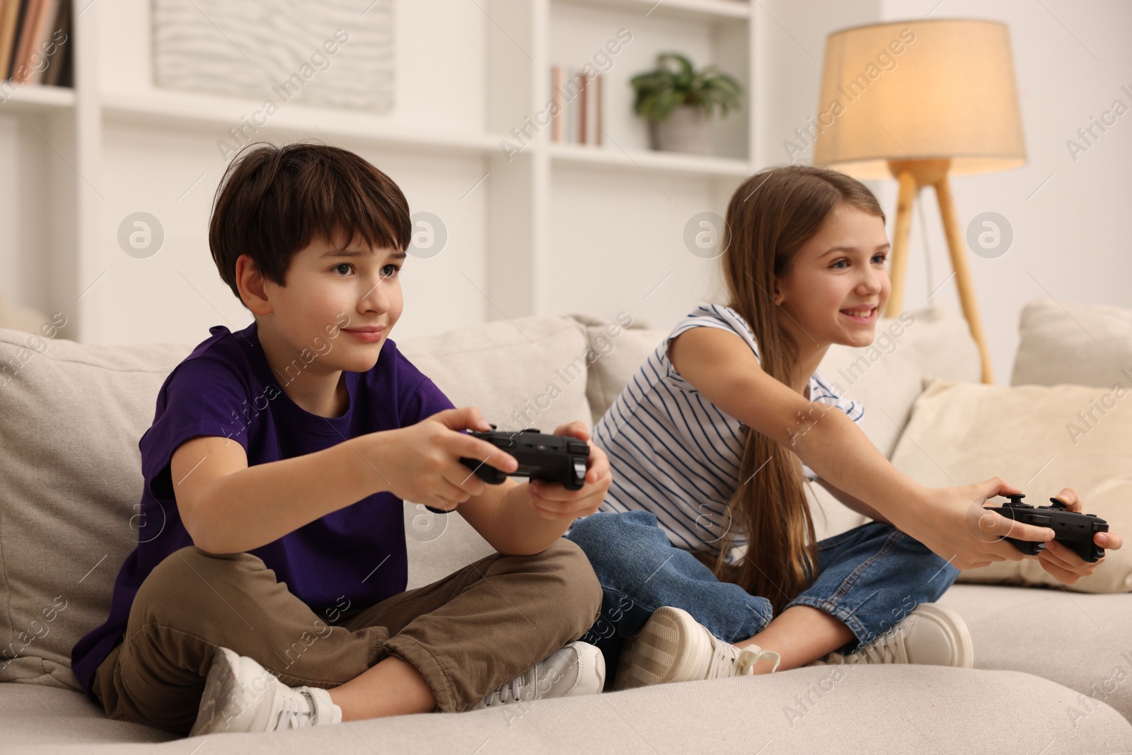 Photo of Cute kids playing video games on sofa in living room