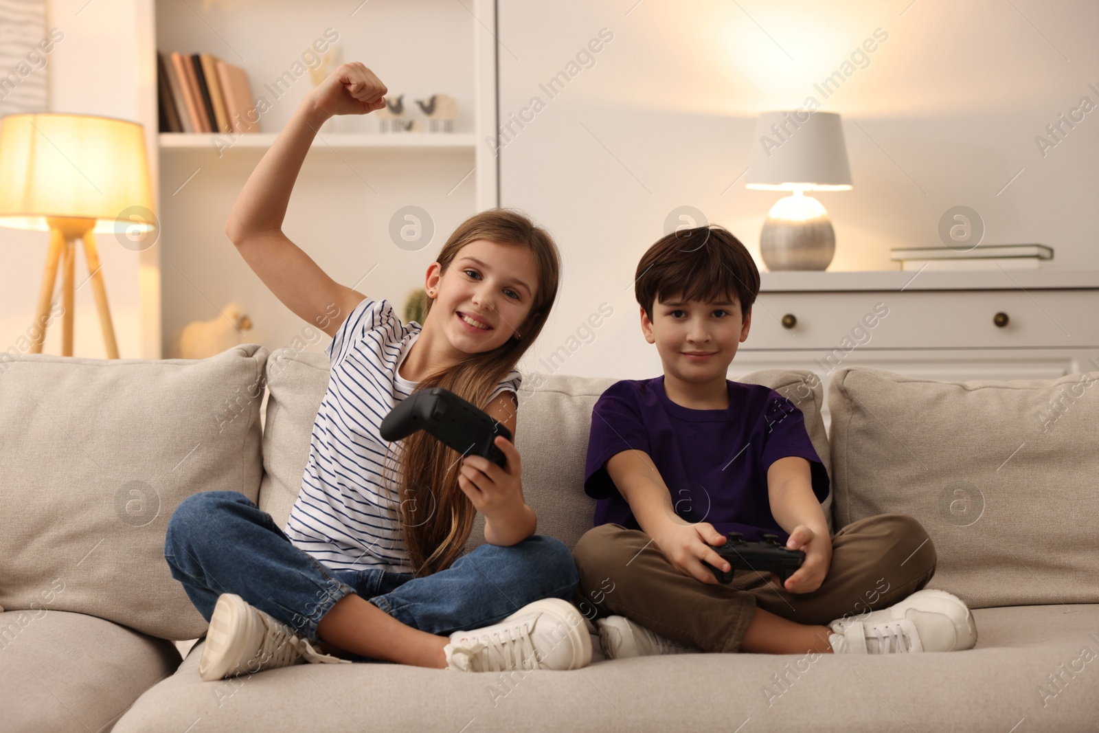 Photo of Cute kids playing video games on sofa in living room