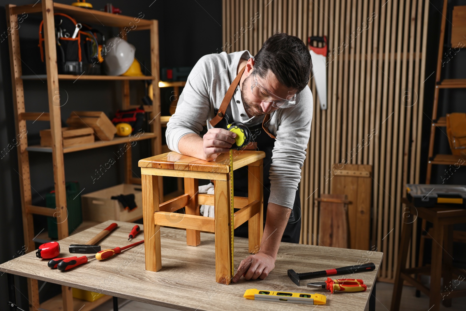 Photo of Repairman measuring wooden stool at table in workshop