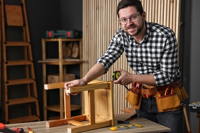 Photo of Repairman measuring wooden stool at table in workshop