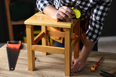 Photo of Repairman measuring wooden stool at table in workshop, closeup