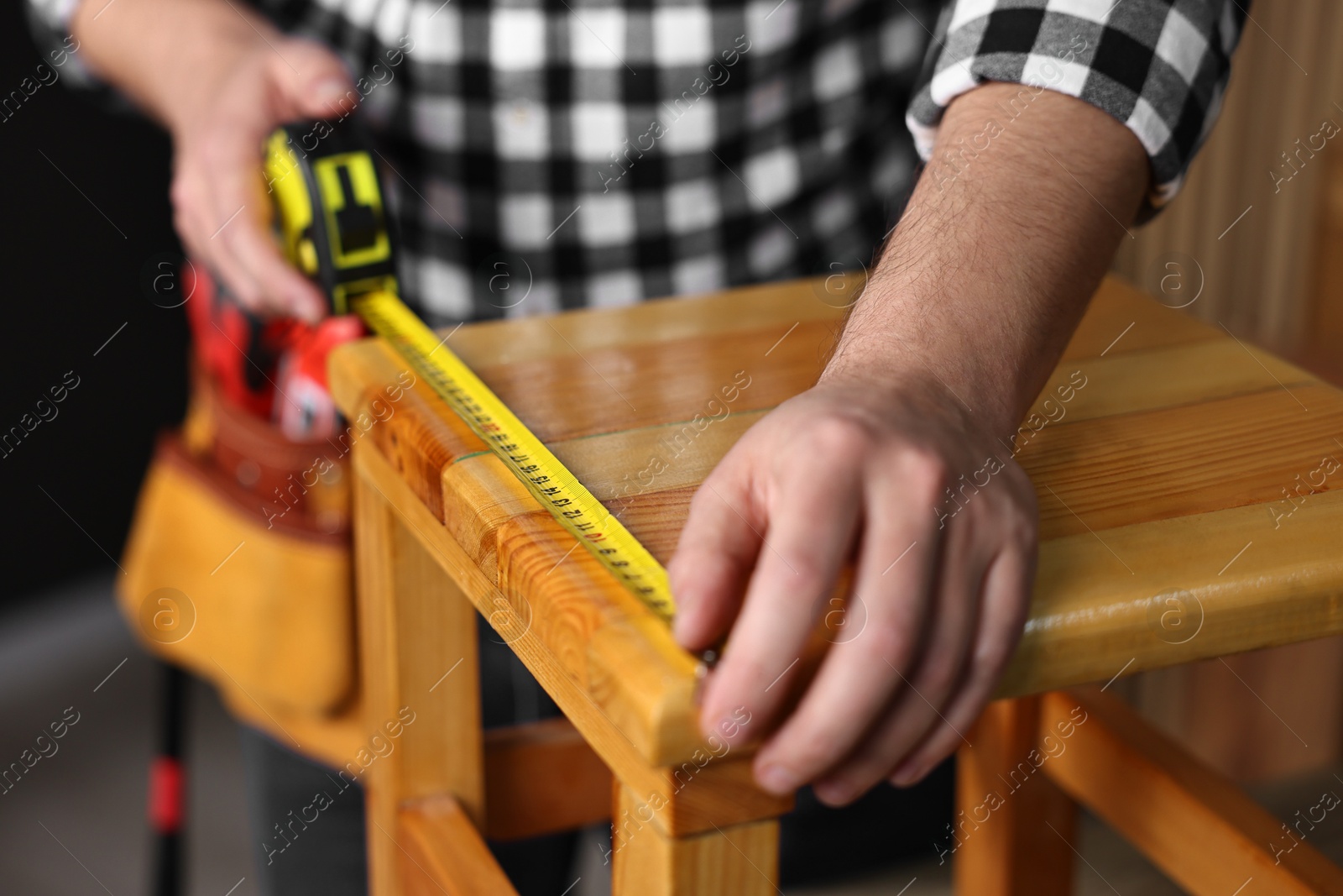 Photo of Repairman measuring wooden stool in workshop, closeup