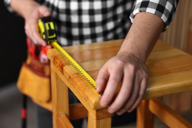 Photo of Repairman measuring wooden stool in workshop, closeup