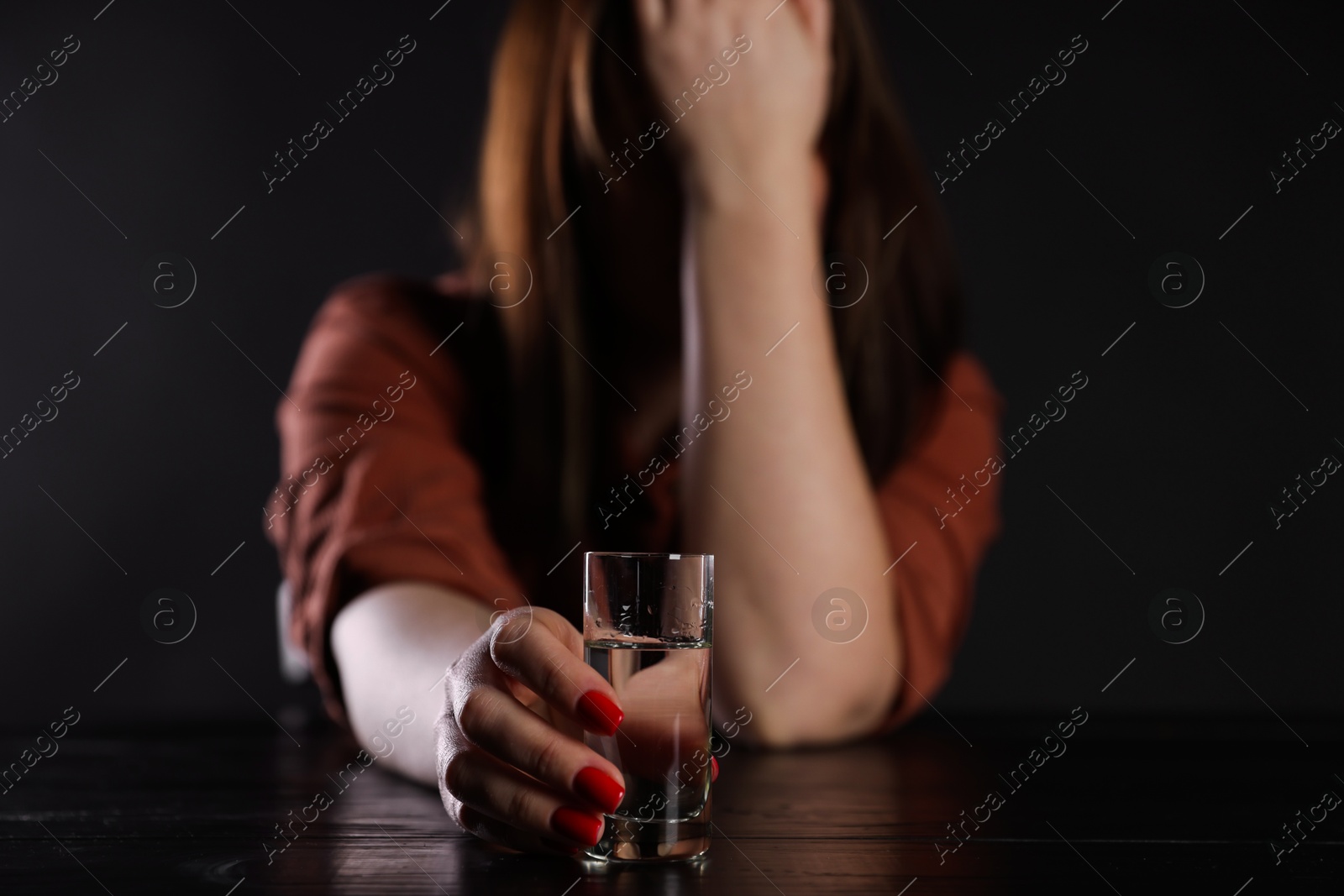 Photo of Alcohol addiction. Miserable woman with vodka at table in dark, selective focus