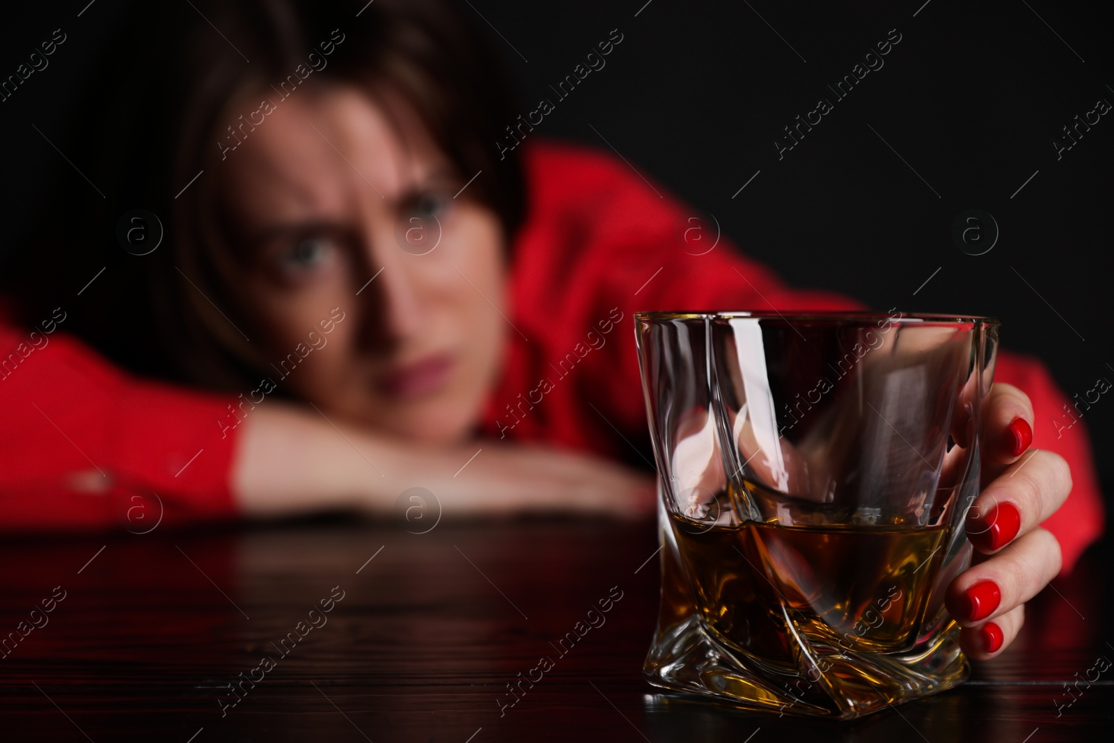 Photo of Alcohol addiction. Miserable woman with whiskey at table in dark, selective focus