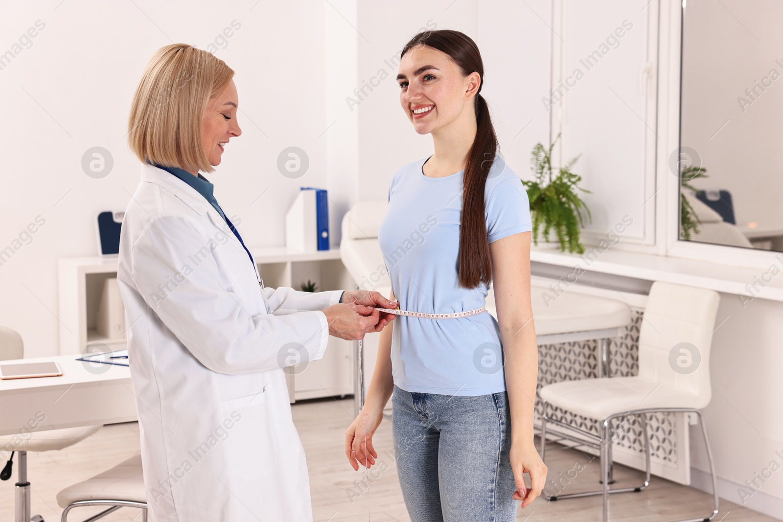 Photo of Happy woman lost weight. Nutritionist measuring patient's waist with tape in clinic