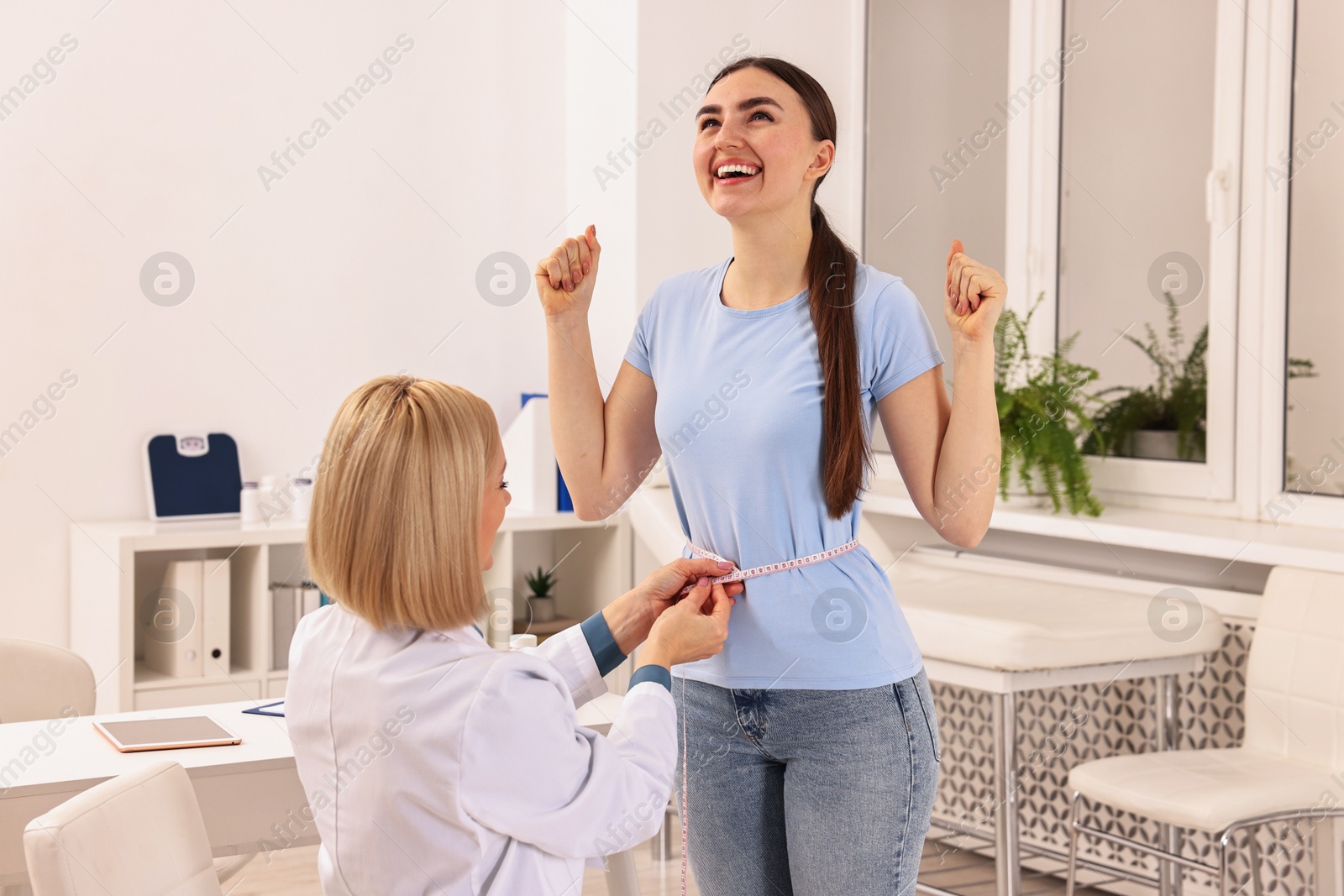 Photo of Happy woman lost weight. Nutritionist measuring patient's waist with tape in clinic