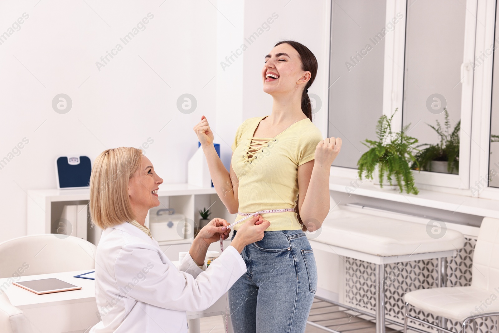 Photo of Happy woman lost weight. Nutritionist measuring patient's waist with tape in clinic