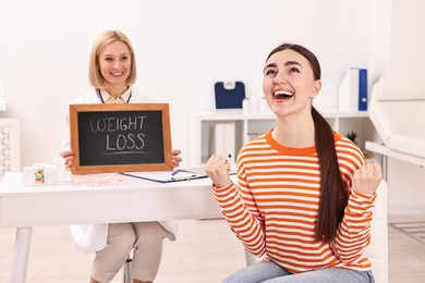 Photo of Happy woman lost weight and nutritionist with small blackboard in clinic, selective focus