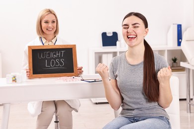 Photo of Happy woman lost weight and nutritionist with small blackboard in clinic