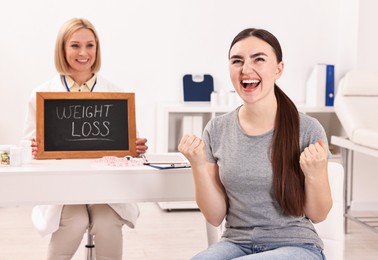 Photo of Happy woman lost weight and nutritionist with small blackboard in clinic