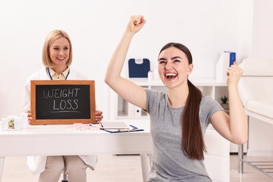 Happy woman lost weight and nutritionist with small blackboard in clinic